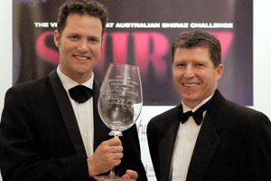 Two men in formal wear with bowties, one holding a glass trophy with an inscription.